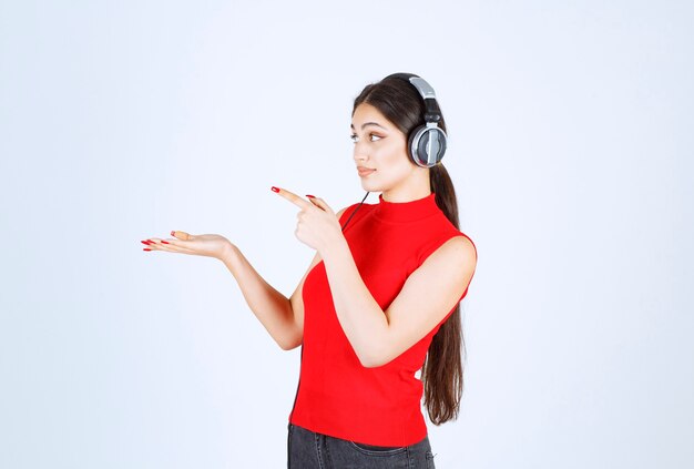 Dj girl in red shirt with headphones pointing something or showing something in her hand.