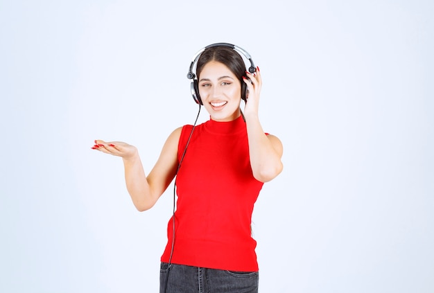 뭔가 가리키는 또는 그녀의 손에 뭔가 보여주는 헤드폰 빨간색 셔츠에 dj 소녀.