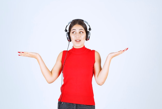 Dj girl in red shirt with headphones pointing something or showing something in her hand.