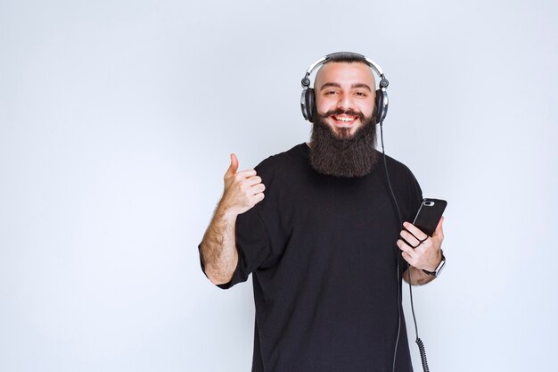 Dj with beard wearing headphones and enjoying the playlist at his phone.