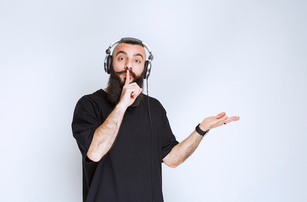 Dj with beard wearing headphones and pointing at right side.