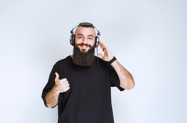 헤드폰을 착용하고 긍정적 인 손 기호를 보여주는 수염을 가진 DJ.