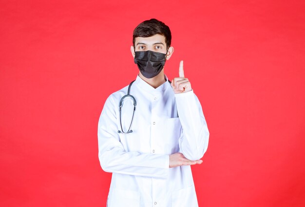 Доктор в черной маске со стетоскопом на шее.
