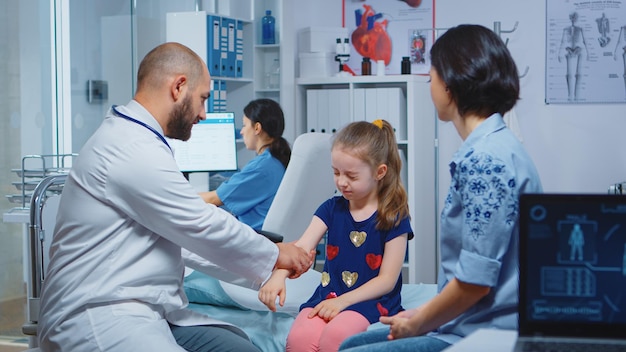 Free photo doctor checking child injured arm and talking with mother. healthcare practitioner physician specialist in medicine providing health care service radiographic treatment examination in hospital cabinet