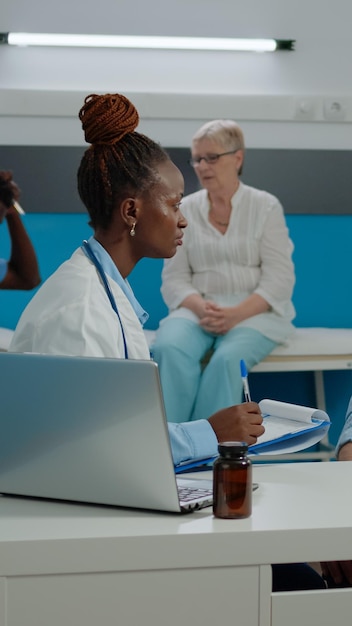 Doctor checking on elder patient healthcare in medical cabinet at treatment facility. Medic consulting old person for checkup appointment while sitting at desk. People talking at clinic