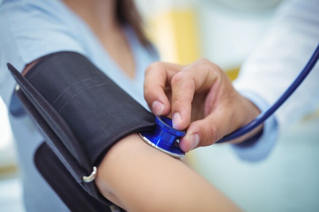 Doctor checking female patient blood pressure