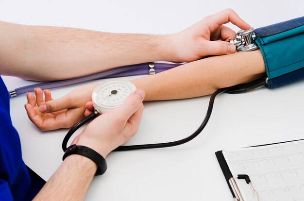 A doctor checking female's patient blood pressure on white desk with medical report on clipboard