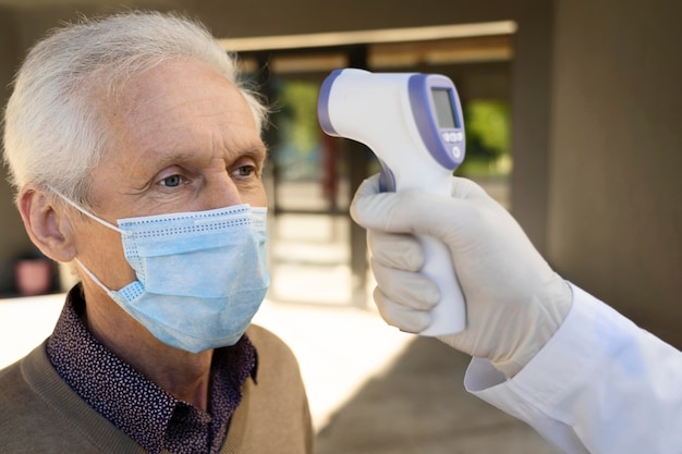 Doctor checking male patient's temperature outside vaccination center