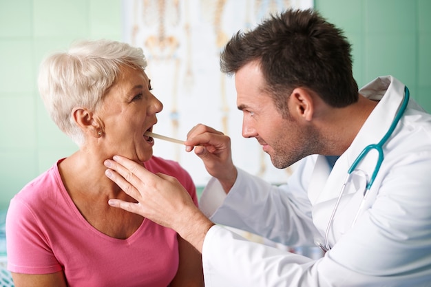 Доктор проверяет горло старшей женщины