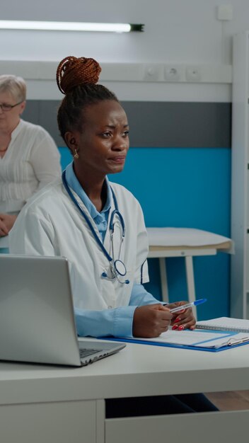 Doctor consulting elder patient with sickness in medical office at clinic. Young medic having conversation with senior person about medicine and healthcare while sitting at desk