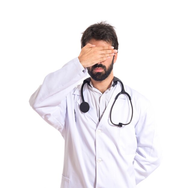 Doctor covering his eyes over isolated white background