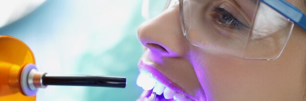 가벼운 근접 촬영을 치료하는 여성 환자의 치아에 빛나는 의사 치과 의사
