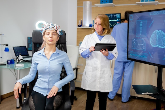 Доктор делает девушке процедуру сканирования мозга в научной лаборатории. Шлем для сканирования мозговых волн