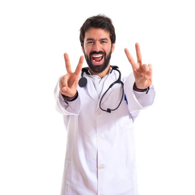 Doctor doing victory gesture over white background