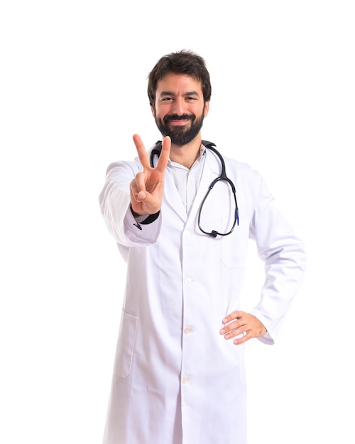 Doctor doing victory gesture over white background