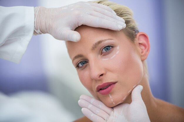 美容治療のために女性患者の顔を調べる医師