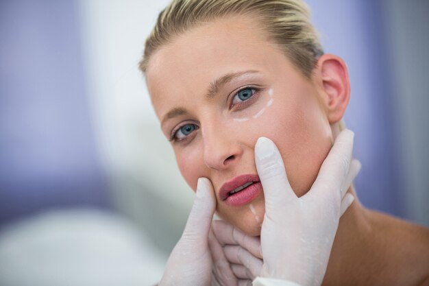 미용 치료를 위해 여성 환자의 얼굴을 검사하는 의사