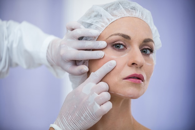 美容治療のために女性患者の顔を調べる医師