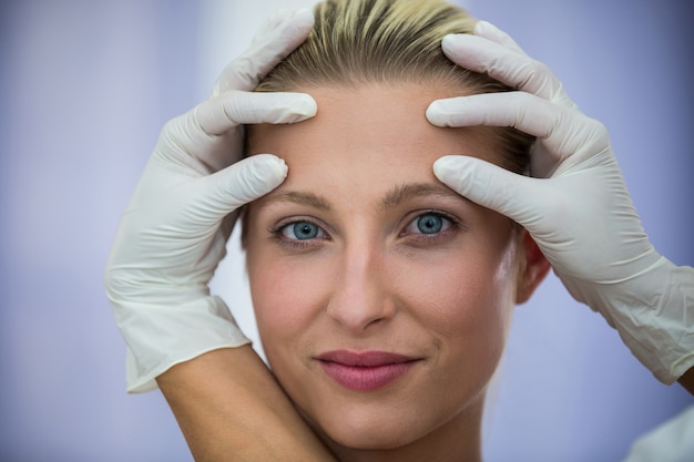 미용 치료에서 여성 환자의 얼굴을 검사하는 의사