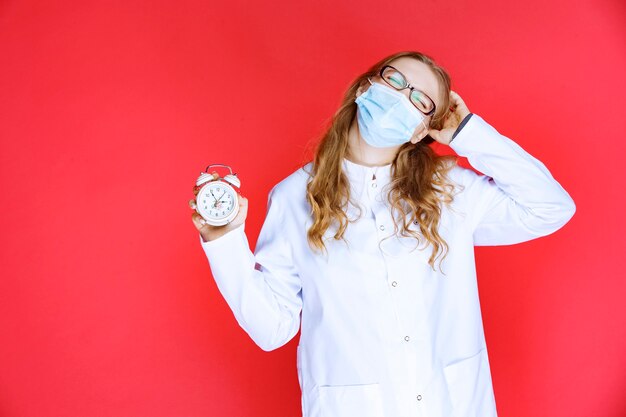 Doctor in face mask holding a clock and looks confused.