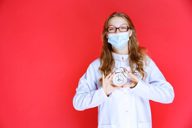 Doctor in face mask showing a clock meaning the time for taking medicines.