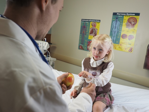 Doctor giving an apple to a little girl in a hospital