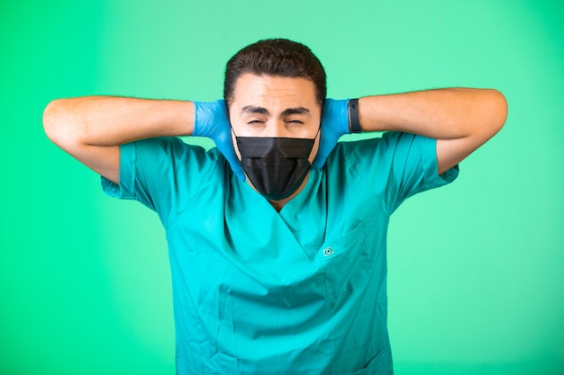 Doctor in green uniform and face mask closing his ears and eyes.