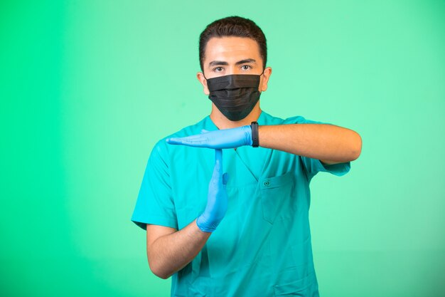 Доктор в зеленой форме и маске делает жесты руками.