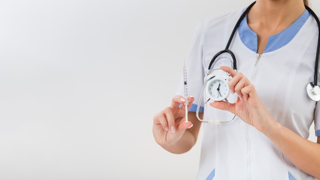 Doctor hands holding a clock and a syringe