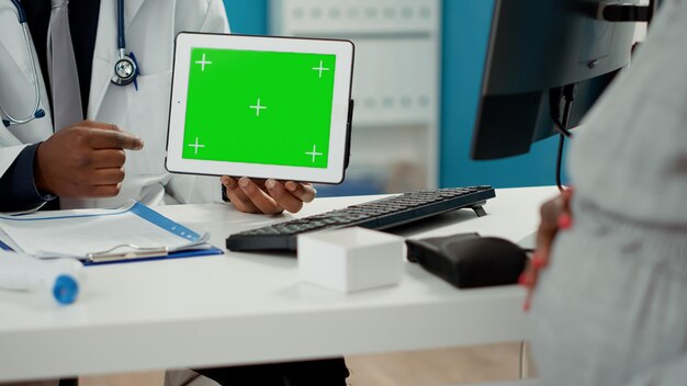 Doctor holding digital tablet with horizontal greenscreen at checkup with expectant person. Male medic working with isolated chroma key template and blank mockup copyspace. Close up.