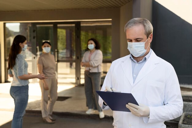 Doctor holding notepad at the vaccination center with patients outdoors