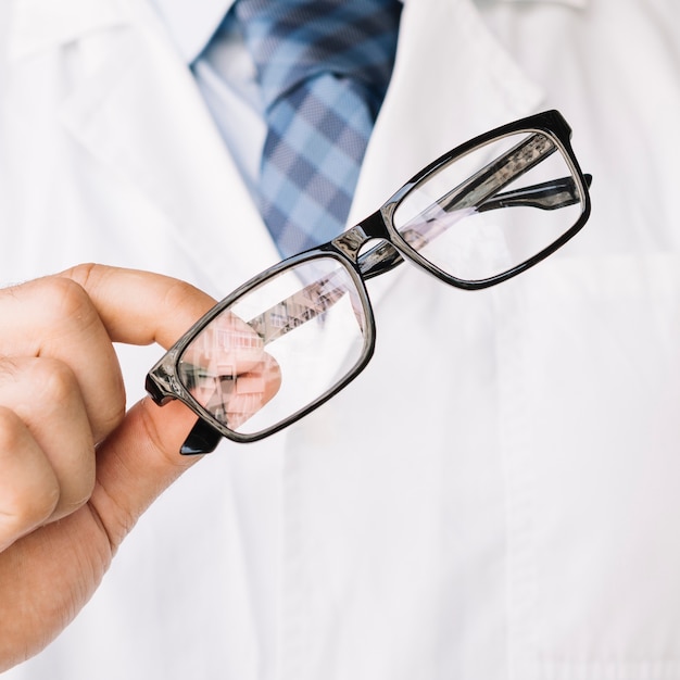 Doctor holding in one hand a pair of black framed glasses