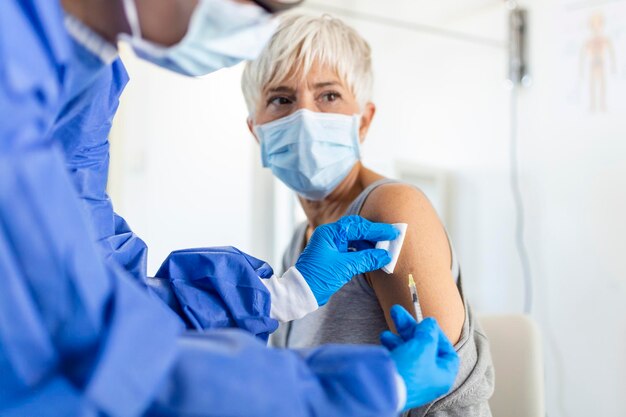 Врач держит шприц, делающий дозу вакцинации covid 19 в плече пациентки в маске Концепция клинических испытаний вакцины против гриппа от гриппа лечение коронирусного вируса крупным планом