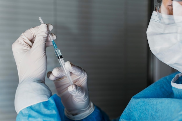 Medico che tiene una bottiglia di vaccino mentre indossa l'equipaggiamento protettivo