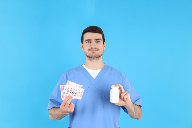 Il dottore tiene il calendario mestruale, gli assorbenti e la bottiglia di pillole su sfondo blu