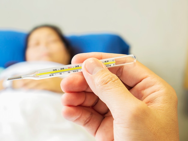 A doctor is looking at thermometer for measuring body temperature of his patient.