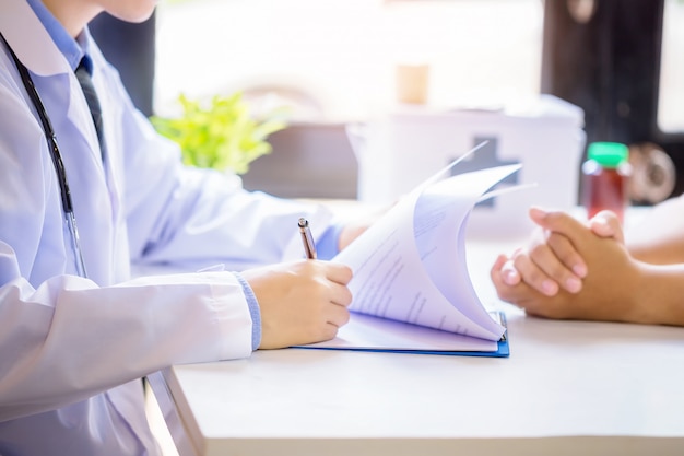 Free photo doctor man consulting patient while filling up an application form at the desk in hospital.