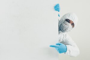 A doctor in mask, gloves and protective suit pointing left and looking