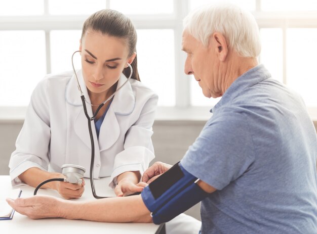 Serious medical worker in white coat and stethoscope writing on clipboard 