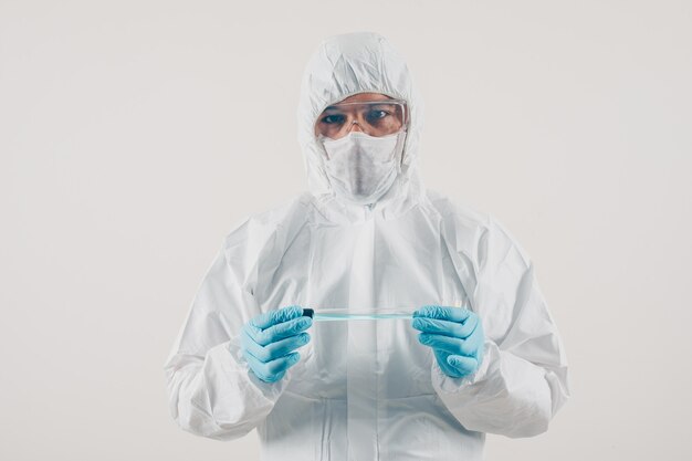 A doctor in medical gloves and protective suit standing and holding medicine in light background. coronavirus