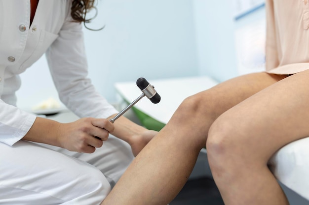 Doctor neurologist knocking on knee of patient with hammer in clinic closeup Diagnosis of neurological pathology of knee reflex concept