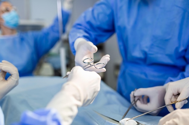 Врач и медицинская бригада медсестер проводят хирургическую операцию в отделении неотложной помощи в больнице, ассистент раздает ножницы и инструменты хирургам во время операции