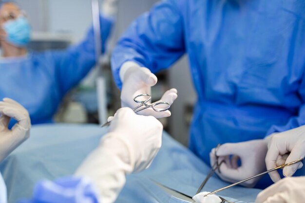 Врач и медицинская бригада медсестер проводят хирургическую операцию в отделении неотложной помощи в больнице, ассистент раздает ножницы и инструменты хирургам во время операции