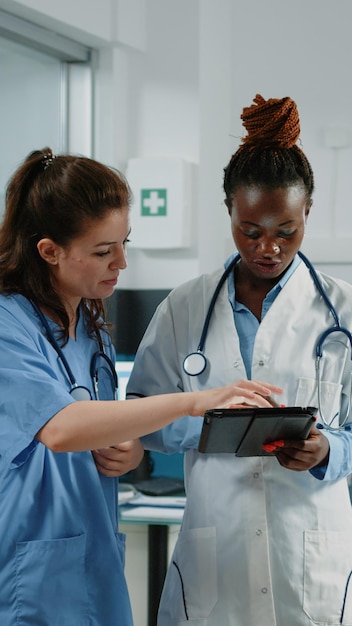 캐비닛의 의료 시스템용 태블릿으로 작업하는 의사와 간호사. 검사 및 치료를 위한 기술을 사용하는 의료진 및 조수의 의료 팀. 의사 사무실의 전문가