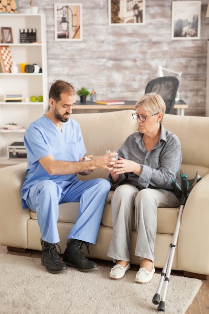 Doctor in nursing home helping senior woman to take her medicine.