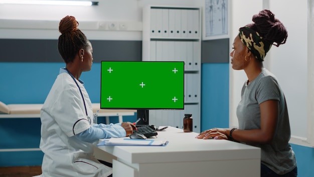 Doctor and patient looking at computer with horizontal green screen in doctors office. Medic and woman using monitor with chroma key and isolated mockup template and background.