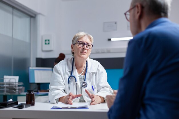 Doctor and patient meeting at consultation appointment to do healthcare checkup in cabinet. Medic talking to aged man about diagnosis and treatment after examination at medical visit