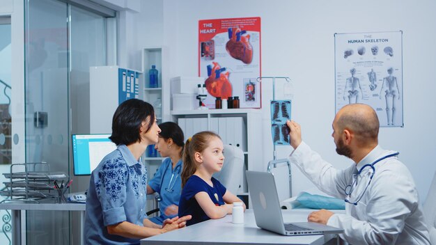Врач и пациенты, глядя на рентгеновский снимок, сидя в медицинском кабинете. Врач-специалист в области медицины, предоставляющий консультации по медицинским услугам, рентгенологическое лечение в больничном кабинете поликлиники