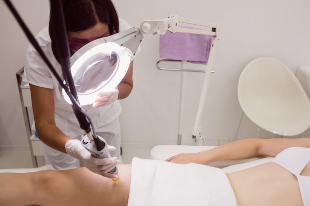 Doctor performing laser hair removal on female patient skin