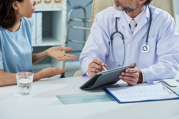 doctor pointing at digital tablet screen while explaining something to the patient